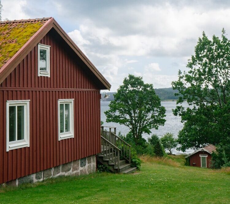 A red house with a green roof next to a body of water